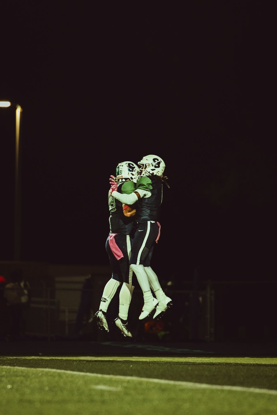 Two football players in team uniforms celebrate by jumping together.