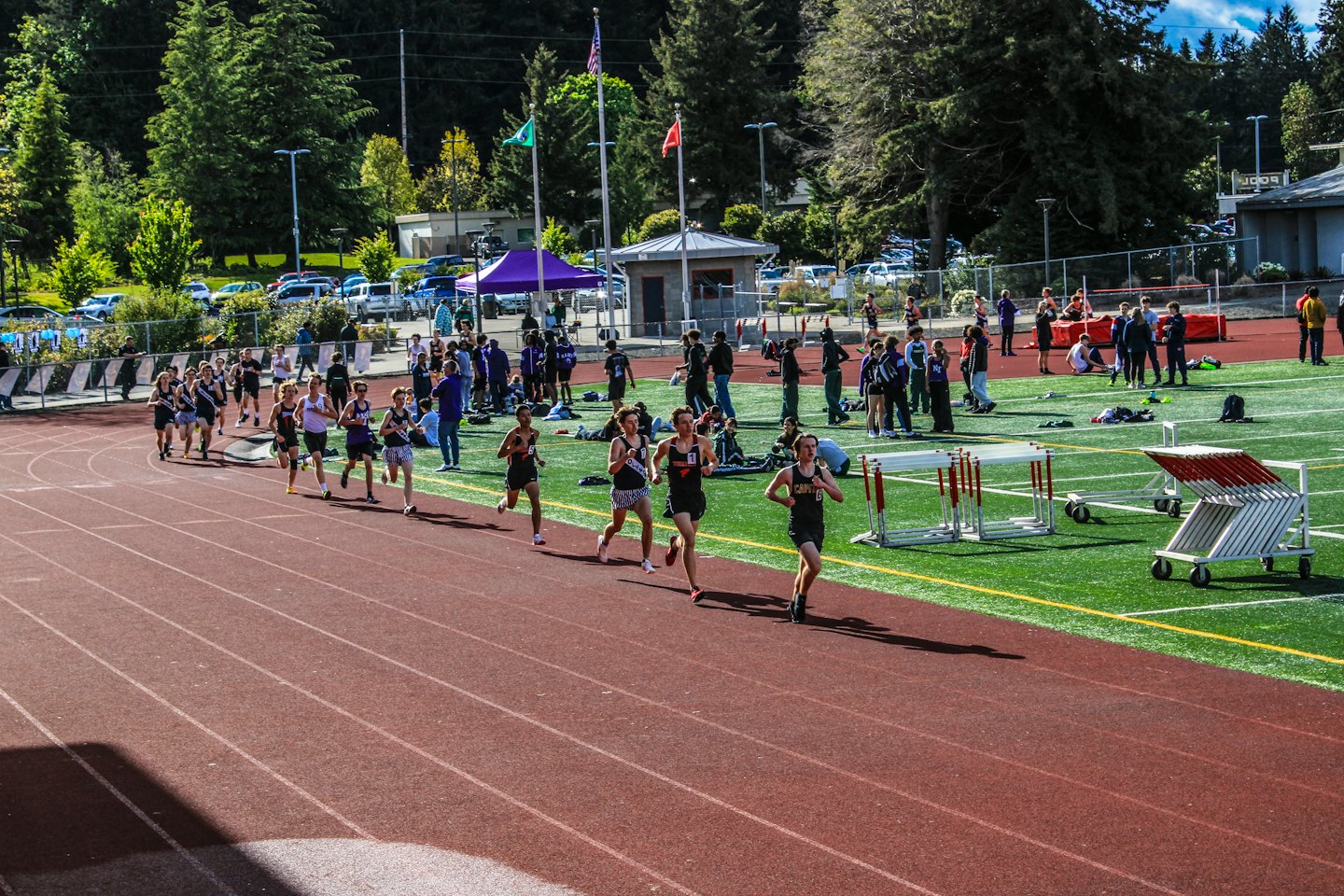 Young athletes race on a track near hurdles.