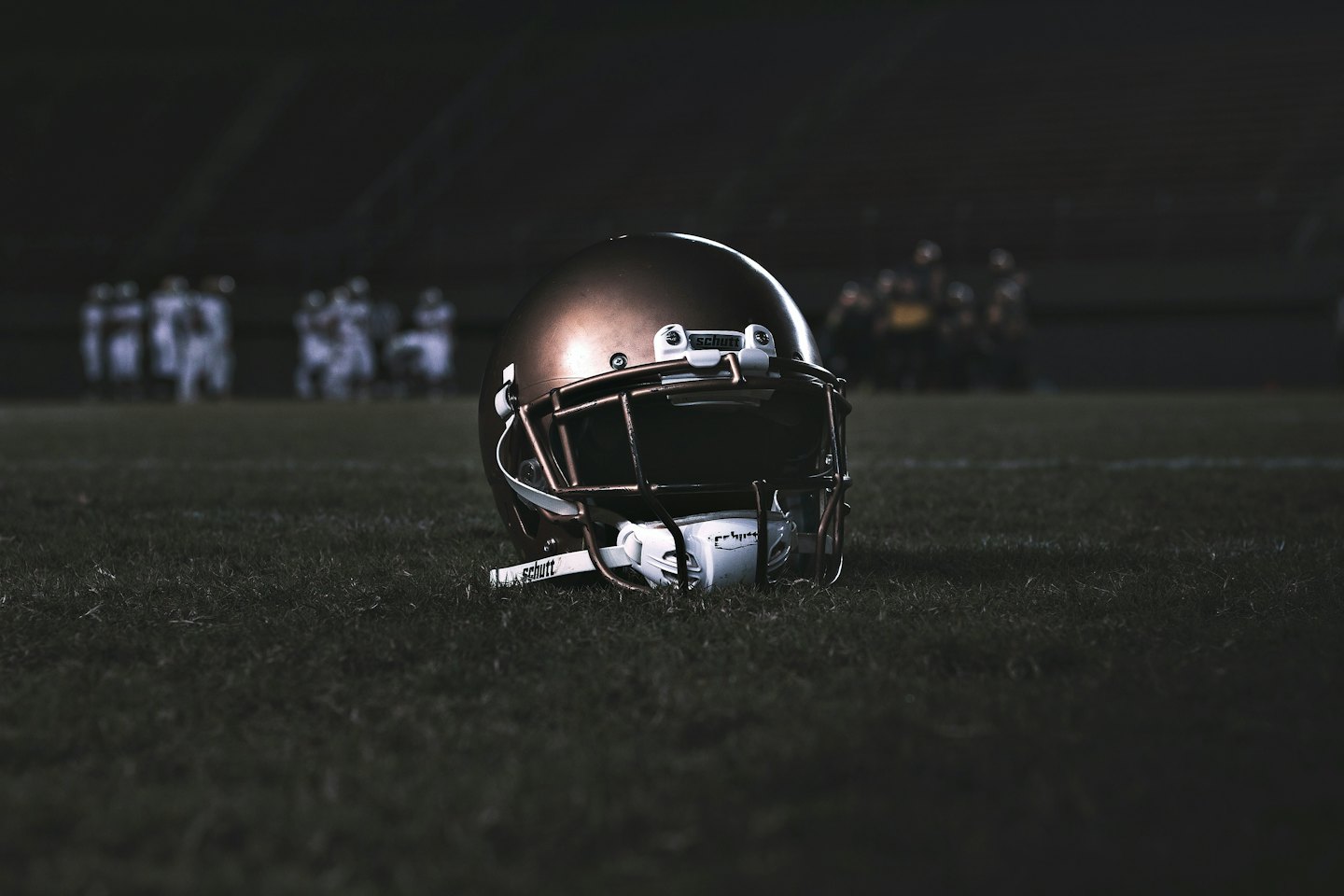 Bronze American football helmet on a green field at night.